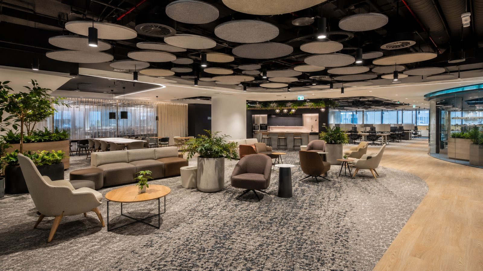 Khu vực lounge và làm việc chung trong văn phòng hiện đại với ghế sofa, trần tiêu âm, cây xanh và thiết kế sang trọng